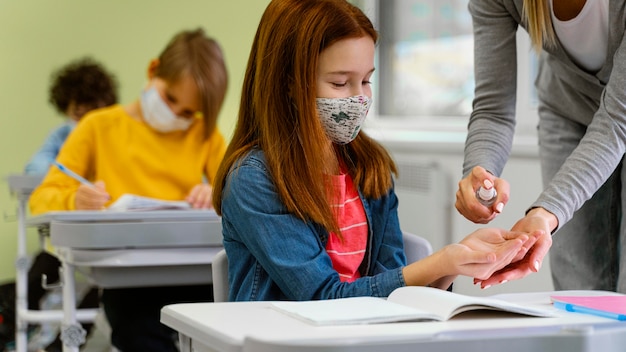 Student mit medizinischer Maske, die Händedesinfektionsmittel vom Lehrer erhält