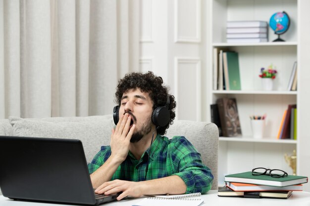 Student online süßer junger Kerl, der am Computer mit Brille im grünen gähnenden Hemd studiert