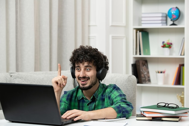 Student online süßer junger Kerl, der am Computer mit Brille im grünen Hemd-Bingo studiert, aufgeregt