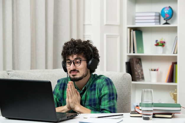 Student online süßer junger Kerl, der am Computer mit Brille im grünen Hemd studiert und betet