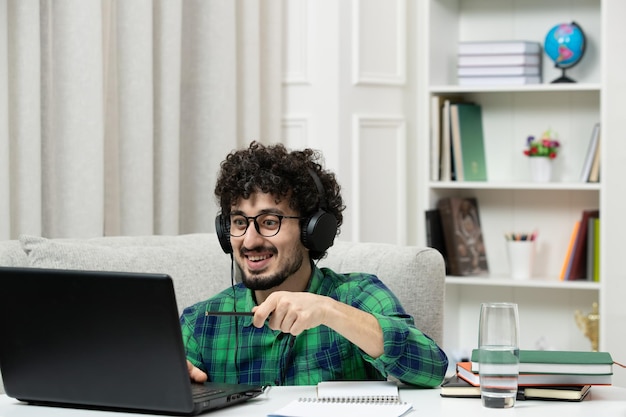 Student online süßer junger Kerl, der am Computer mit Brille im grünen Hemd studiert und glücklich aussieht