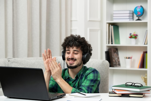 Student online süßer junger Kerl, der am Computer mit Brille im grünen Hemd studiert und in die Hände klatscht