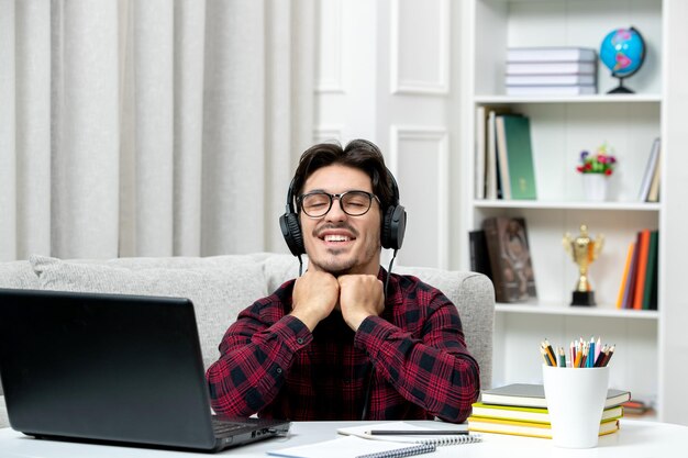 Student online süßer Kerl in kariertem Hemd mit Brille, der am Computer studiert, glücklich schließende Augen