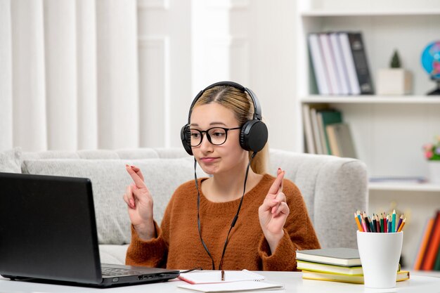 Student online süßes Mädchen in Brille und Pullover, das am Computer studiert und die Daumen drückt