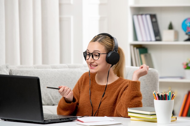 Student online süßes Mädchen in Brille und Pullover, das am Computer studiert und glücklich lächelt