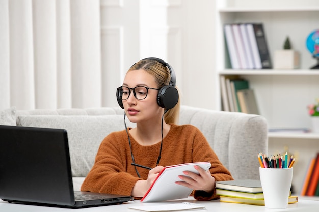 Student online süßes Mädchen in Brille und Pullover, das am Computer studiert und Notizen schreibt