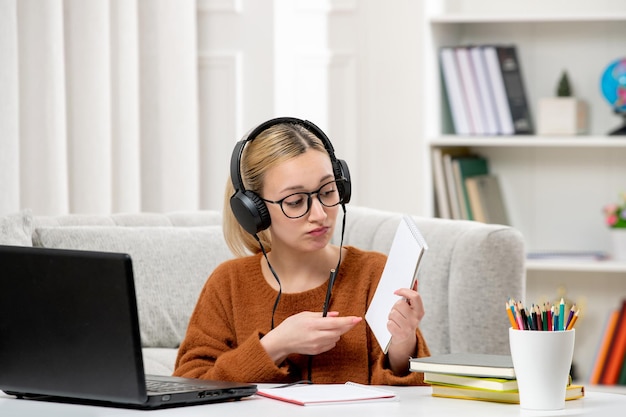 Student online süßes Mädchen in Brille und Pullover, das am Computer studiert und Notizen zeigt