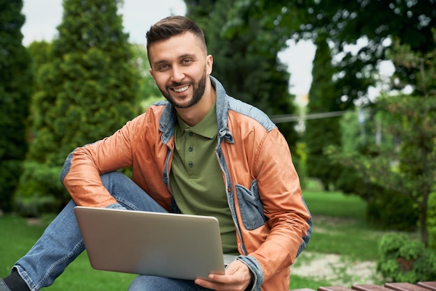 Student posiert mit Laptop im grünen Garten