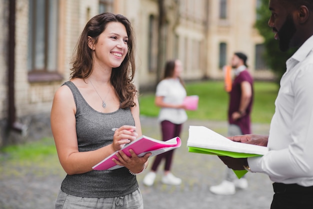 Kostenloses Foto studenten stehen draußen lächelnd halten notebooks