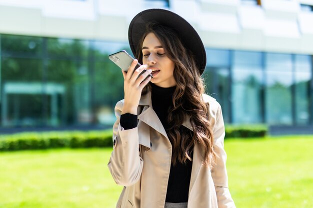 Studentin der Schönheit, die mit dem Freisprech-System des Smartphones spricht, während sie einen Ordner auf dem Campus der Universität hält.