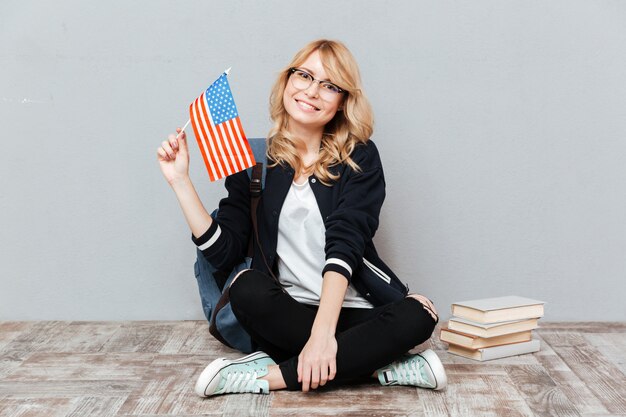 Studentin, die Flagge von USA hält, die auf dem Boden sitzt