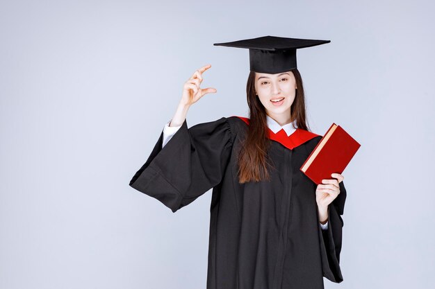 Studentin im akademischen Kleid, das rotes Buch hält. Foto in hoher Qualität