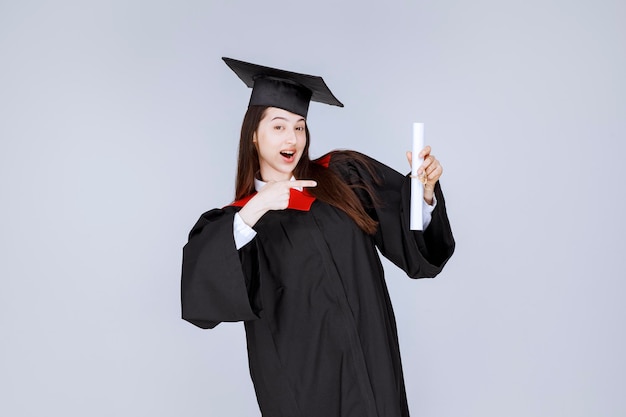 Studentin im Aufbaustudium im Kleid mit College-Zertifikat glücklich. Foto in hoher Qualität