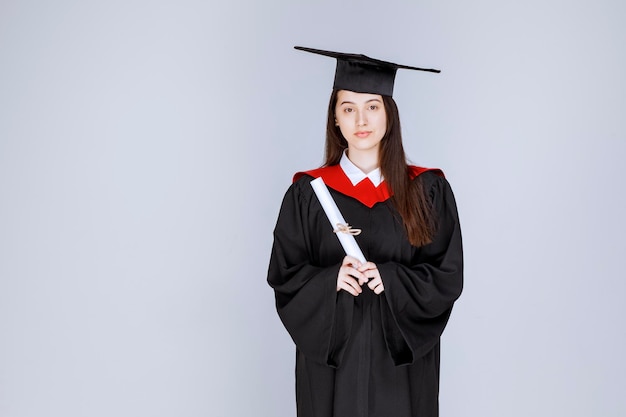 Studentin im Aufbaustudium im Kleid mit College-Zertifikat posiert. Foto in hoher Qualität
