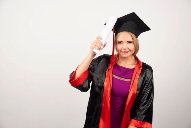 Studentin im Kleid, das Diplom auf Weiß hält.