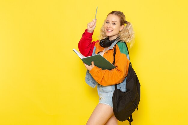 Studentin jung in moderner Kleidung, die Heft mit Lächeln auf Gelb hält