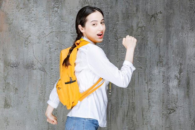 Studentin mit gelbem Rucksack, der auf ihrer Seite steht. Foto in hoher Qualität