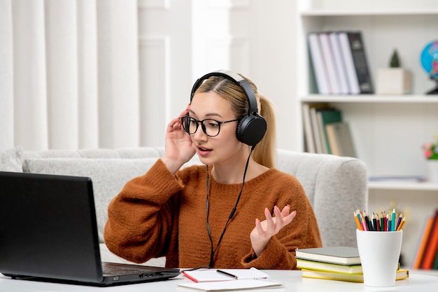 Kostenloses Foto studentin online, junges süßes mädchen mit brille und orangefarbenem pullover, das computer studiert und dem unterricht zuhört