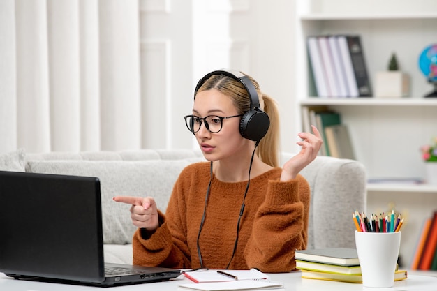 Kostenloses Foto studentin online, junges süßes mädchen mit brille und orangefarbenem pullover, das konzentriert am computer studiert