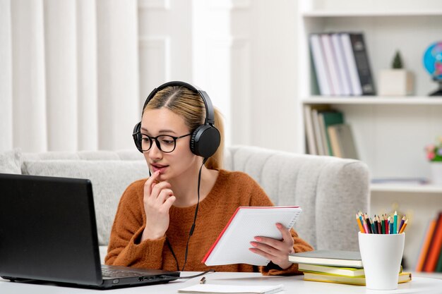 Studentin online süßes Mädchen in Brille und Pullover, das am Computer beißendem Finger studiert