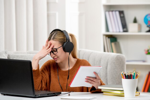 Studentin online süßes Mädchen mit Brille und Pullover, das am Computer studiert und verwirrt den Kopf hält