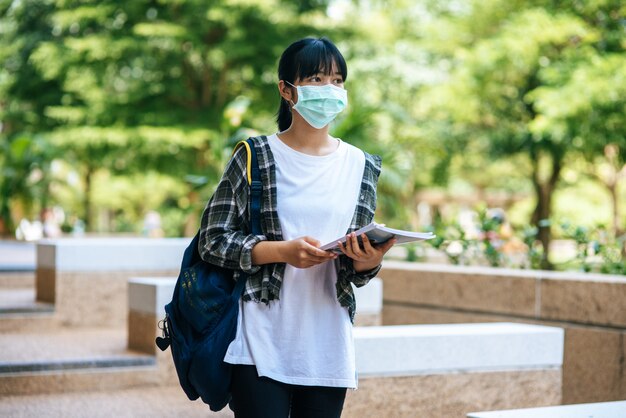 Studentinnen tragen Masken, stehen auf Treppen und halten Bücher.