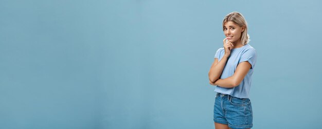 Kostenloses Foto studio-aufnahme von unsicherem, albernem und unsicherem süßem, weiblichem mädchen mit blonden haaren, das halb umgedreht steht