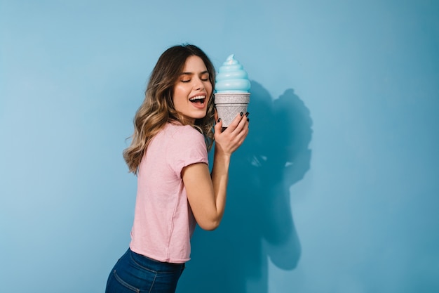 Studioaufnahme der aufgeregten Frau mit Eiscreme lokalisiert auf blauer Wand
