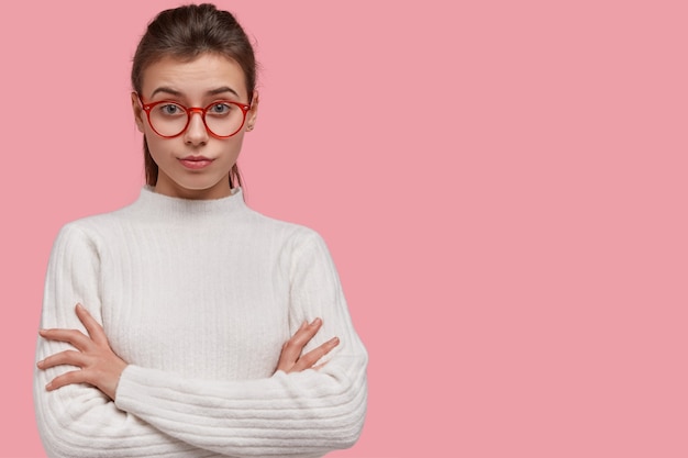 Studioaufnahme der hübschen Frau sieht mit aufmerksamem Gesichtsausdruck aus, drückt die Hände, trägt Pullover