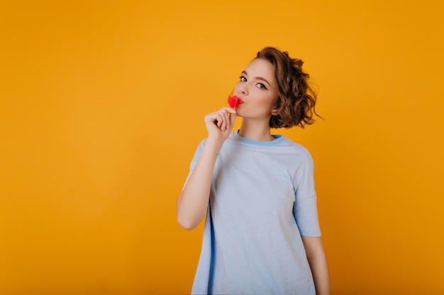 Kostenloses Foto studioaufnahme des hübschen weißen mädchens, das kleines rotes herz hält. innenfoto der frau mit eleganter lockiger frisur, die vor valentinstag kühlt.