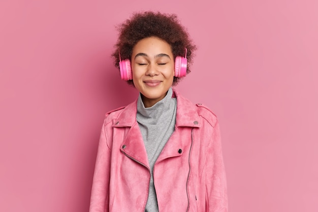 Kostenloses Foto studioaufnahme einer erfreuten jungen afroamerikanerin genießt angenehme melodie hält die augen geschlossen und hört musik über kopfhörer