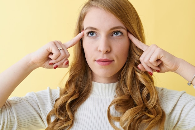 Kostenloses Foto studioaufnahme einer intelligenten nachdenklichen, ernsten jungen frau, die die finger an den schläfen hält und mit nachdenklichem ausdruck aufblickt, versucht, sich an einige wichtige informationen zu erinnern oder über eine entscheidung nachzudenken