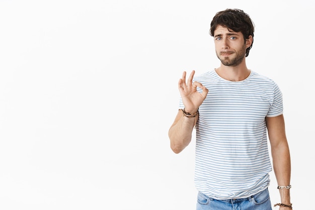 Studioaufnahme eines unter druck gesetzten und müden, unsicheren jungen europäischen männlichen kollegen, der eine gute geste zeigt, während er die lippen schürzt und sich beunruhigt und unwohl fühlt, sich auf etwas unangenehmes und störendes zu einigen. platz kopieren