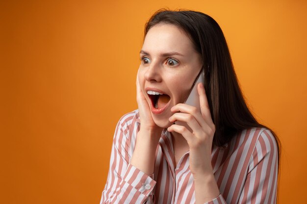 Studiofoto einer jungen Frau, die vor gelbem Hintergrund telefoniert