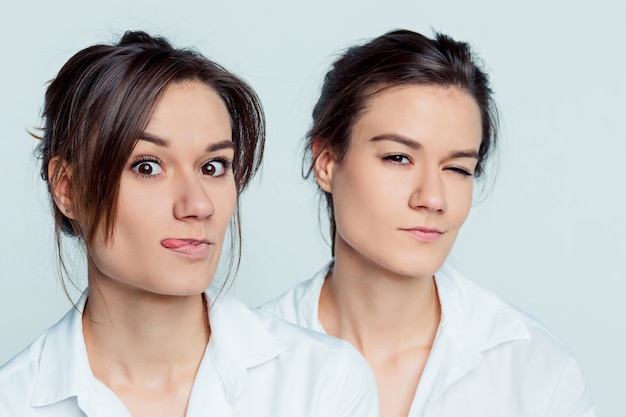 Studioporträt der jungen weiblichen Zwillingsschwestern auf Grau