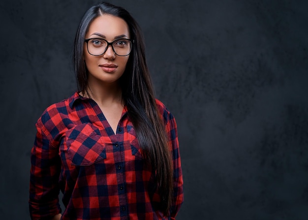 Studioporträt einer brünetten Frau mit Brille, die in einem roten Hemd über grauem Hintergrund gekleidet ist.