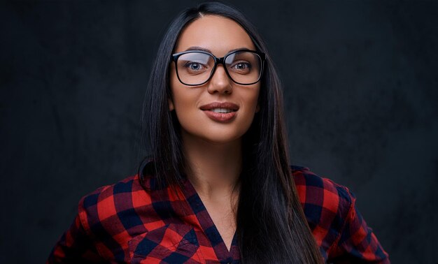Studioporträt einer brünetten Frau mit Brille, die in einem roten Hemd über grauem Hintergrund gekleidet ist.