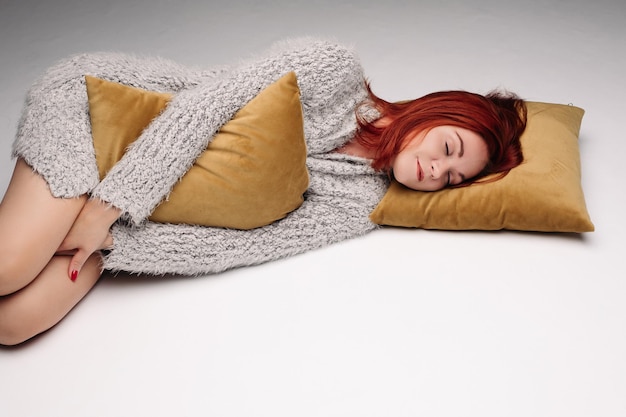 Studioporträt einer Frau in einem Pullover, der ein Kissen umarmt