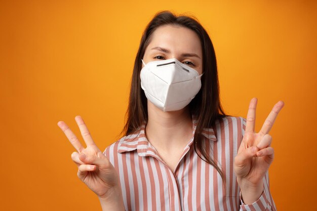 Studioporträt einer jungen schönen Frau, die eine medizinische Gesichtsmaske vor gelbem Hintergrund trägt