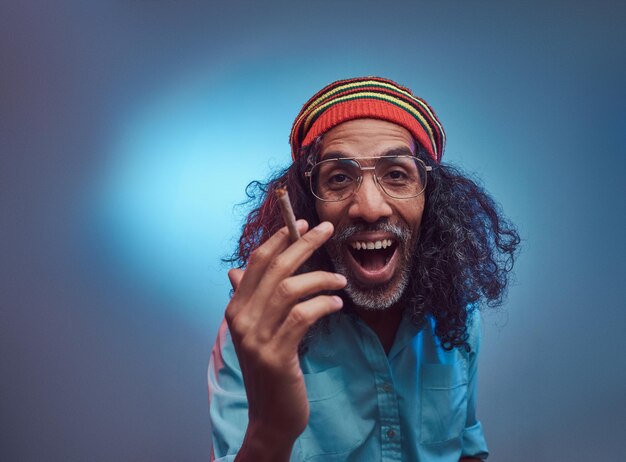 Studioporträt eines afrikanischen Rastafari-Männchens, das Zigaretten raucht. Isoliert auf blauem Hintergrund.