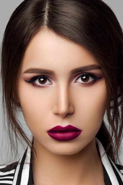 Studioporträt eines attraktiven brünetten Modells mit perfekter Haut und professionellem Abend-Make-up, das eine sexy schwarz-weiß gestreifte Jacke über einem BH auf grauem Hintergrund trägt