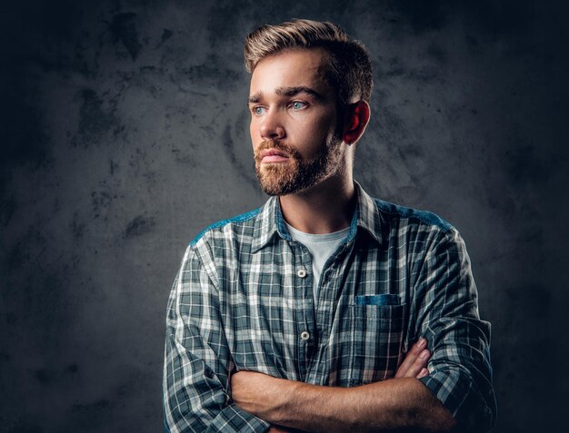 Studioporträt eines blauäugigen, bärtigen Hipster-Männchens mit verschränkten Armen auf grauem Hintergrund.