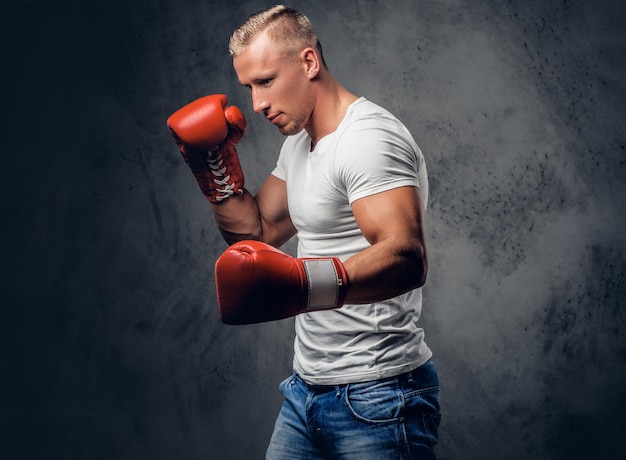 Studioporträt eines blonden Kämpfers mit roten Boxhandschuhen, Kleidern in einem weißen T-Shirt auf grauem Hintergrund.