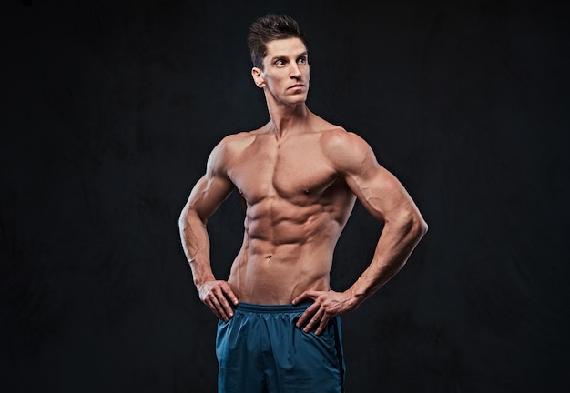 Studioporträt eines hemdlosen Mannes mit ektomorphem Muskel über dunkelgrauem Hintergrund.