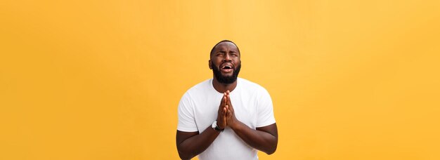 Studioporträt eines jungen afrikanisch-amerikanischen Mannes in weißem Hemd, der im Gebet die Hände hält und auf die