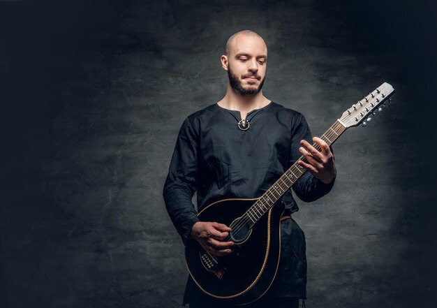 Studioporträt eines Mannes in traditioneller keltischer Kleidung, der auf Mandoline über grauem Vignettenhintergrund spielt.