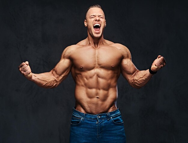 Studioporträt eines muskulösen Mannes mit nacktem Oberkörper in Jeans auf grauem Hintergrund.