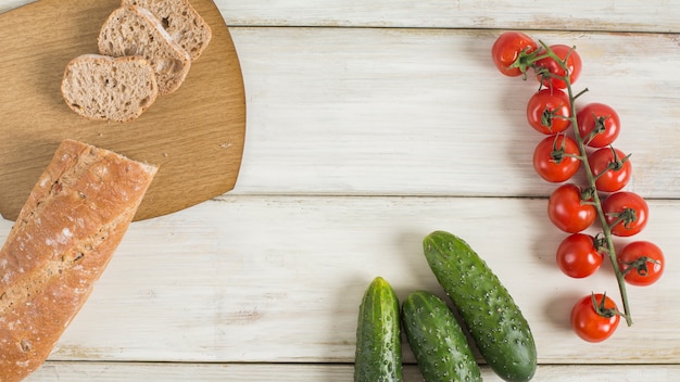 Stück Baguette; Gurken- und Kirschtomaten auf Schreibtisch aus Holz