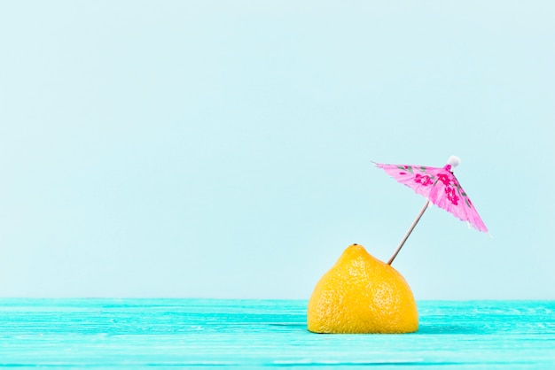 Stück gelbe Zitrone mit rosa Regenschirm auf die Oberseite auf blauem Hintergrund