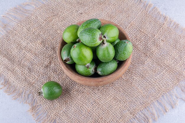 Stück Stoff unter einer kleinen Schüssel Feijoas auf Marmorhintergrund. Foto in hoher Qualität